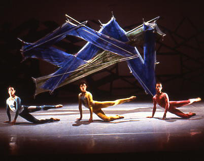 A group of dancers posing in front of a large piece of art.