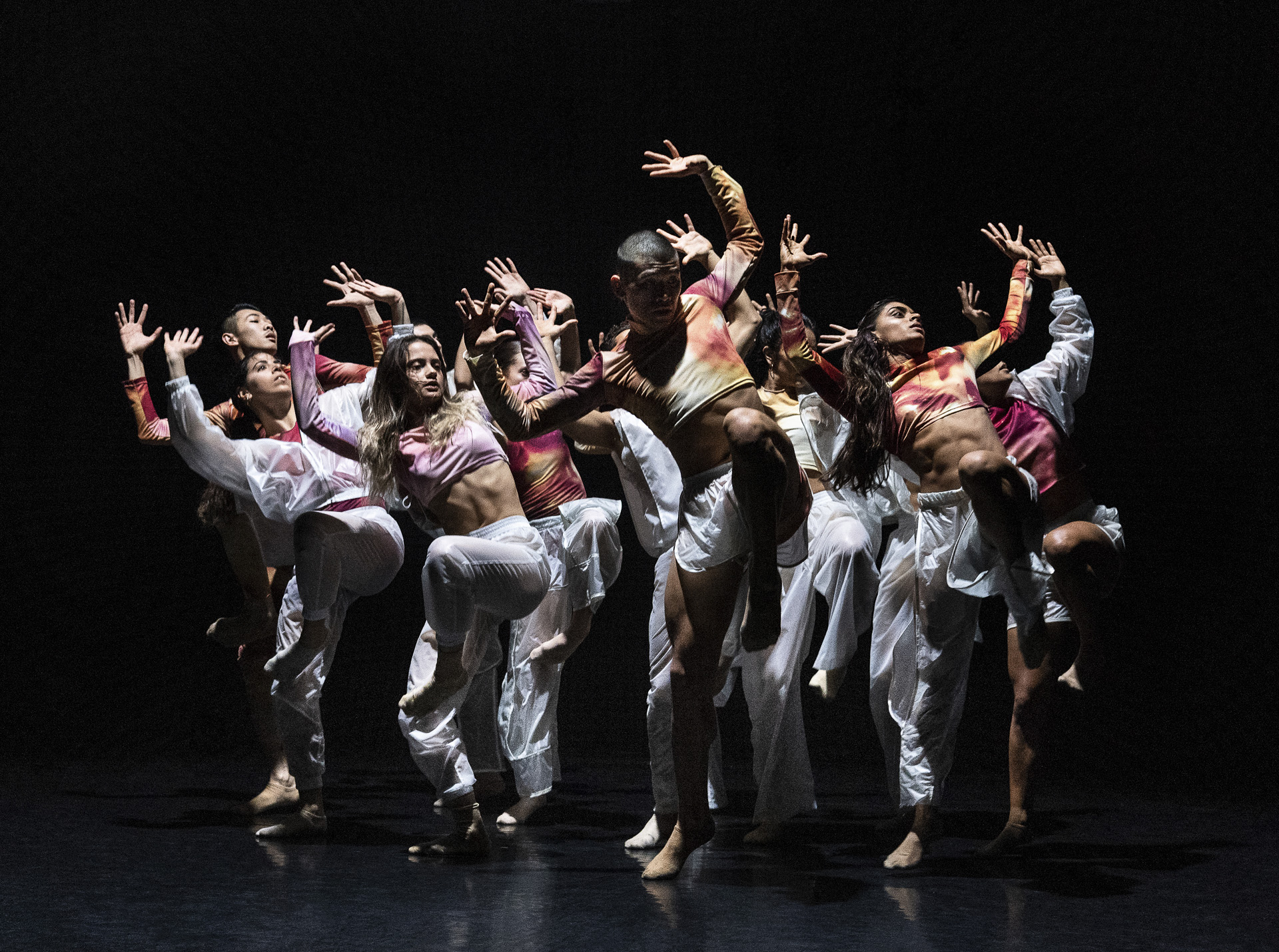 A group of dancers performing on a dark stage.