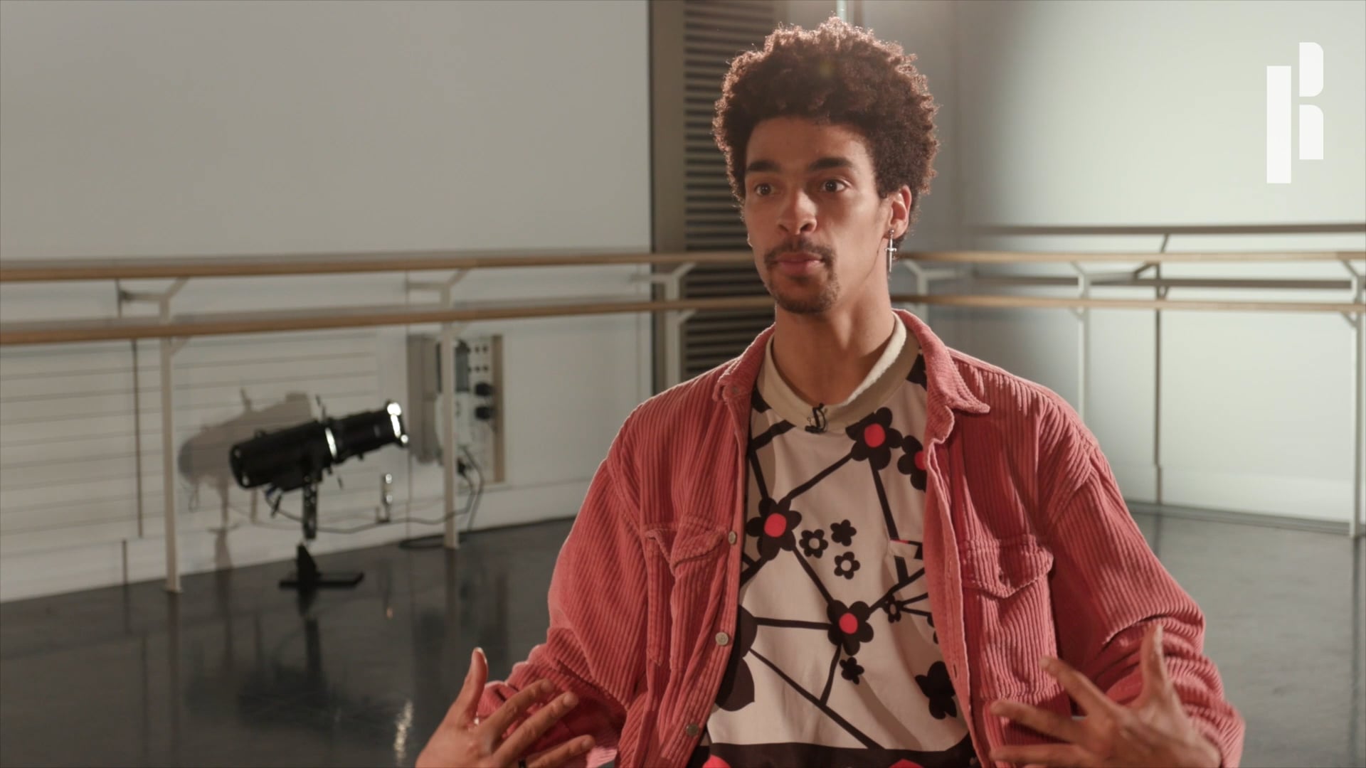 A young man in a pink jacket standing in a dance studio.