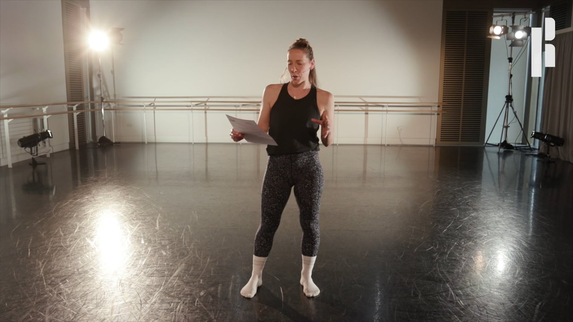 A woman standing in a dance studio holding a piece of paper.