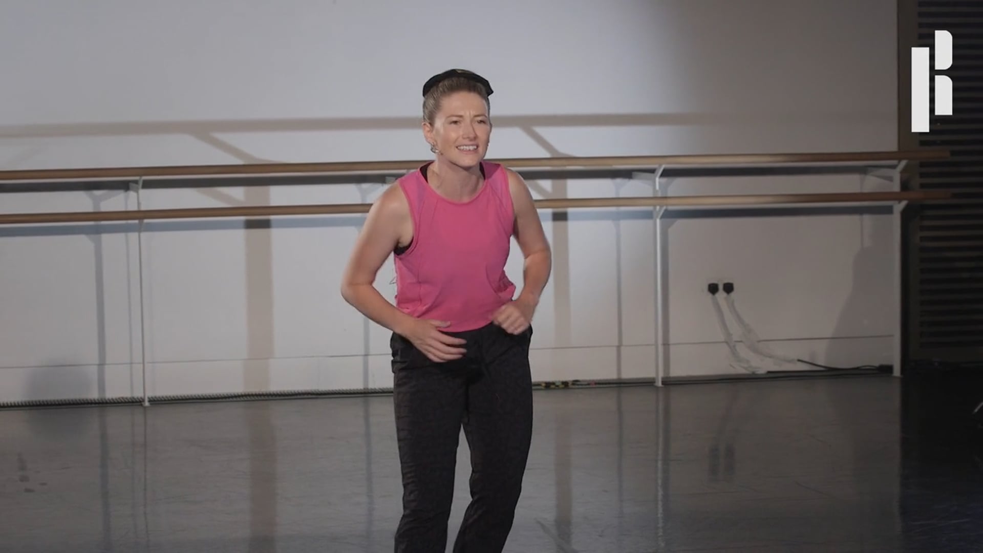 A woman in a pink top standing in a dance studio.