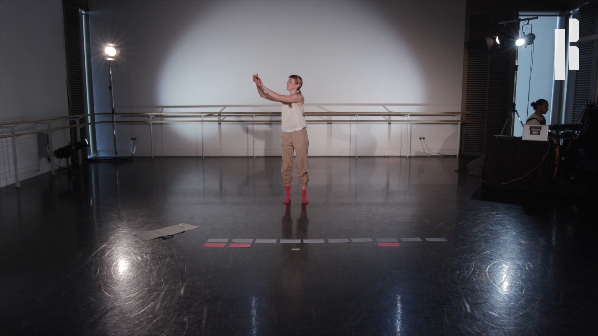 A dancer is standing on a white floor in a dance studio.