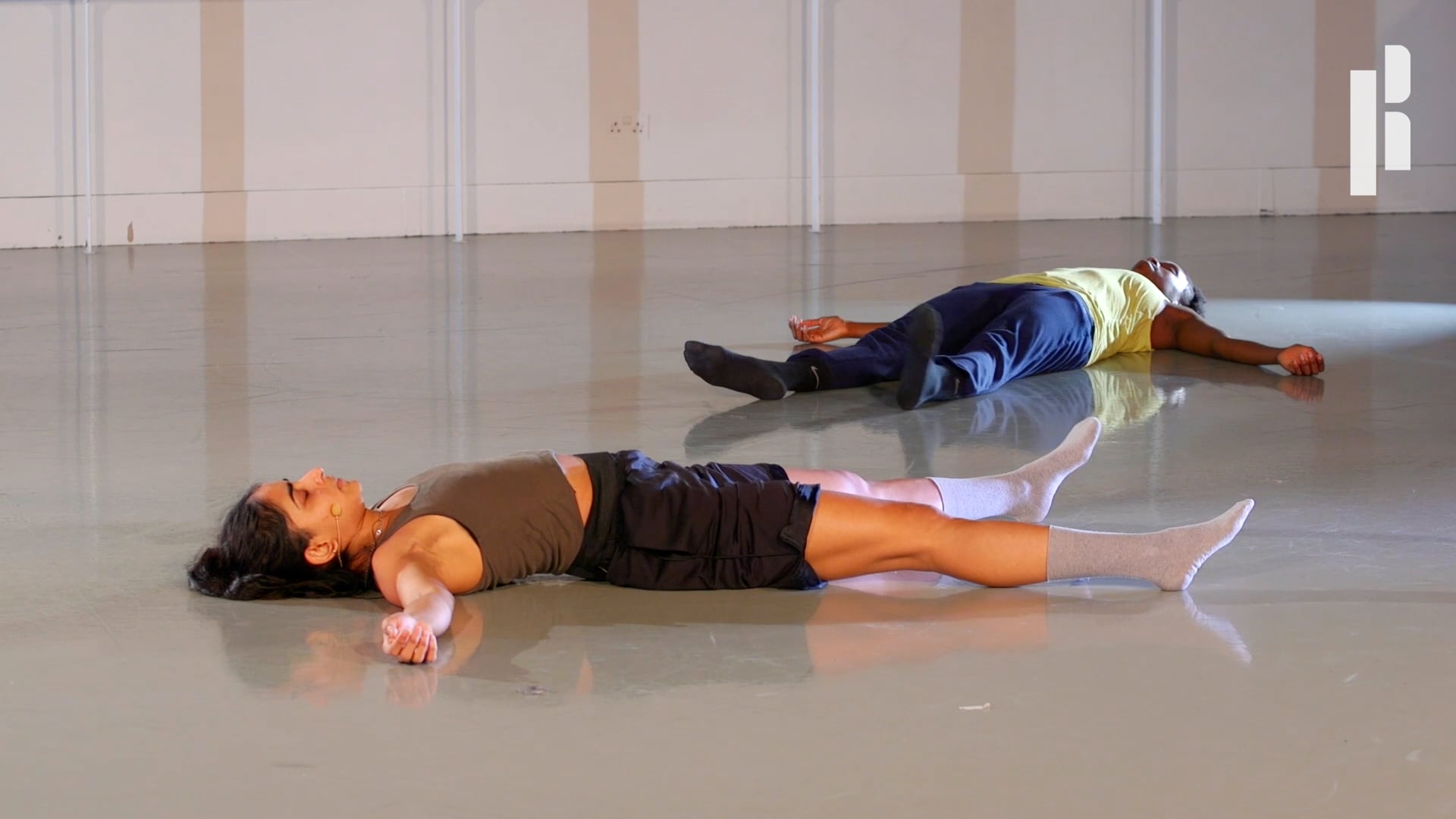 Two people laying on the floor in a dance studio.