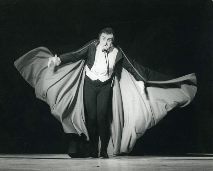 A man in a tuxedo and cape on stage.