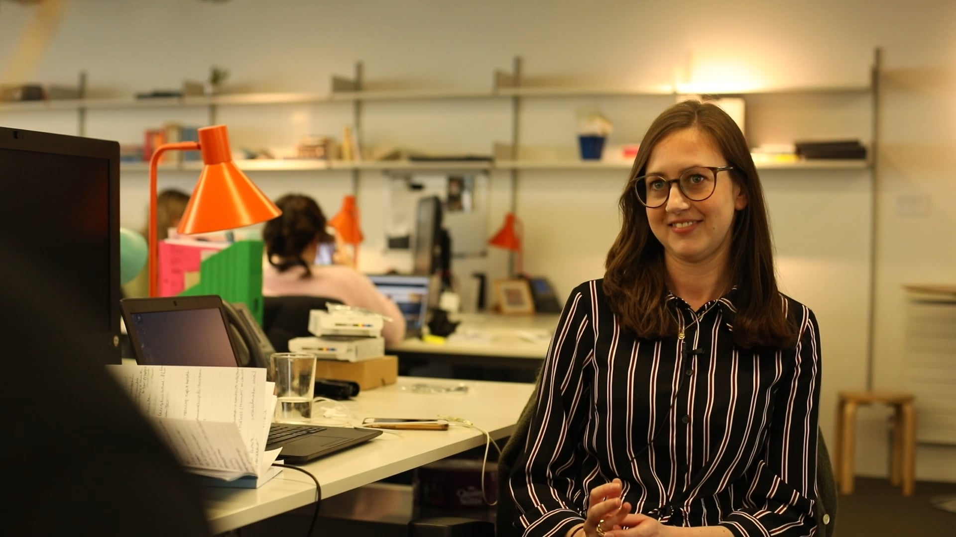 A woman in glasses sitting at a desk in an office.