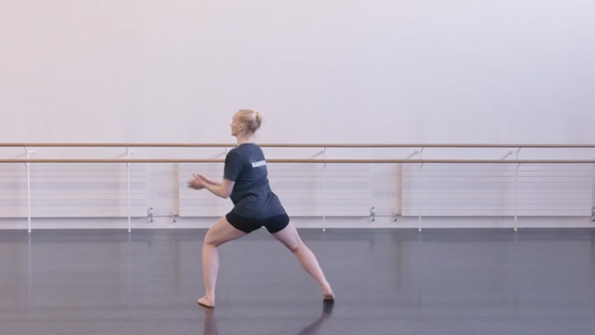 A woman in a black top and shorts is standing in a dance studio.