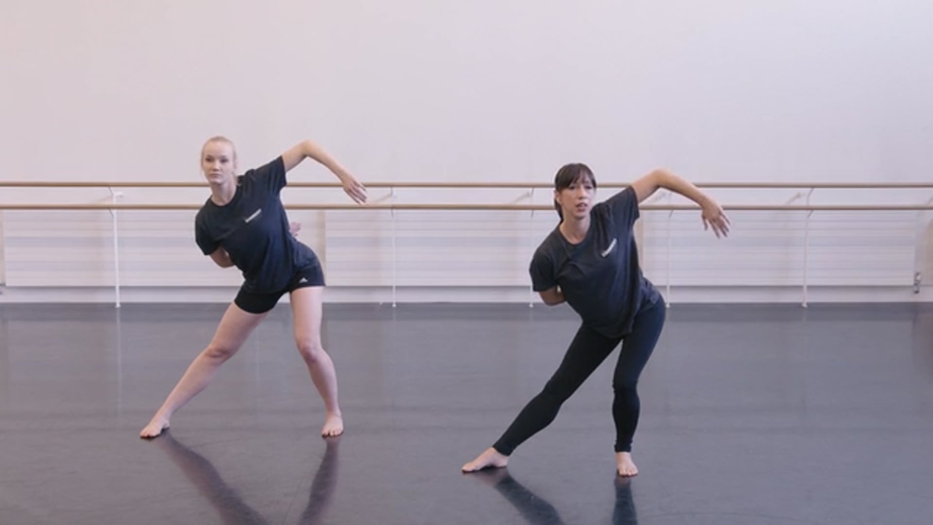 Two dancers in black shirts are standing in a dance studio.