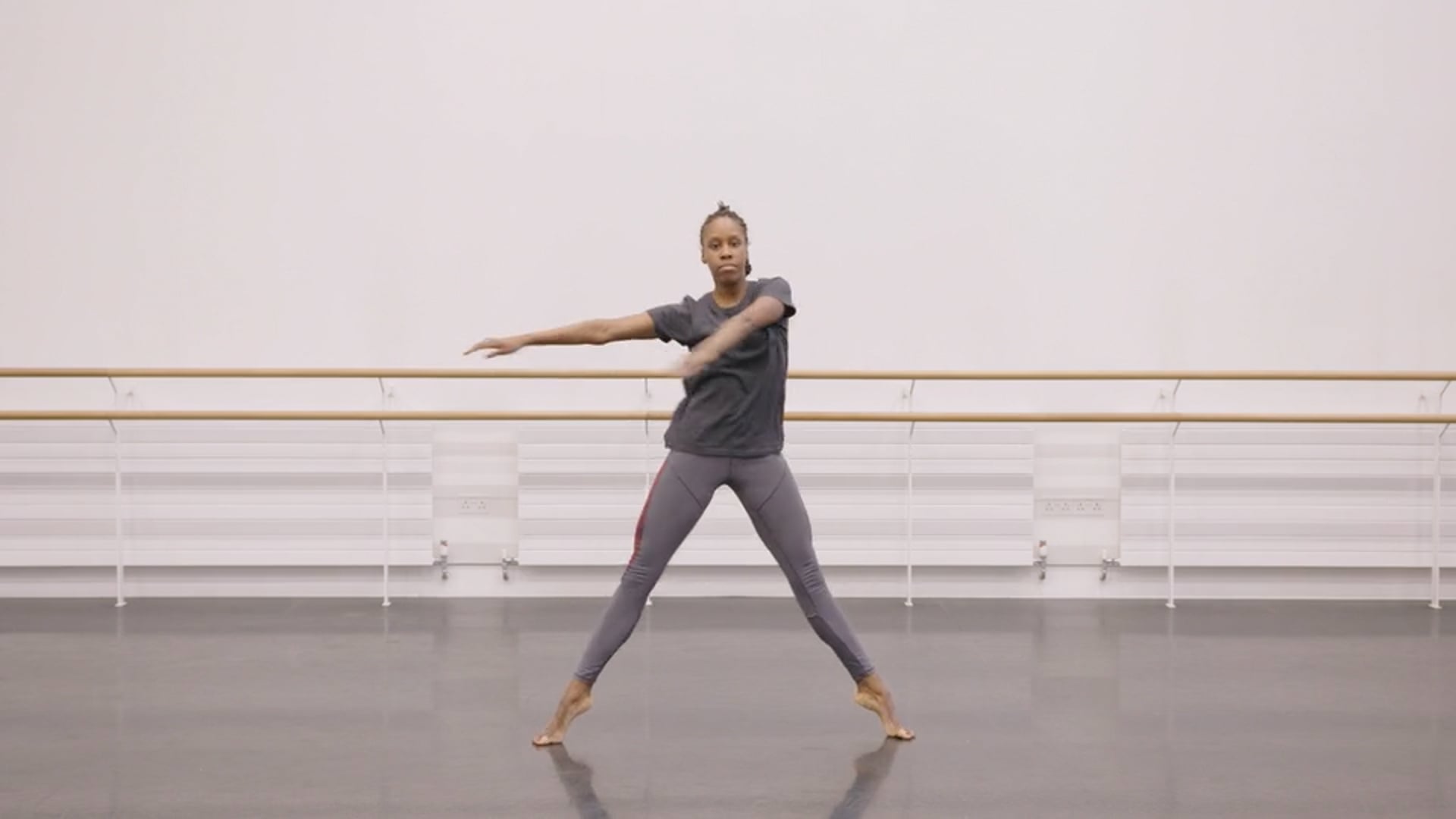 A woman in a gray shirt is standing in a dance studio.