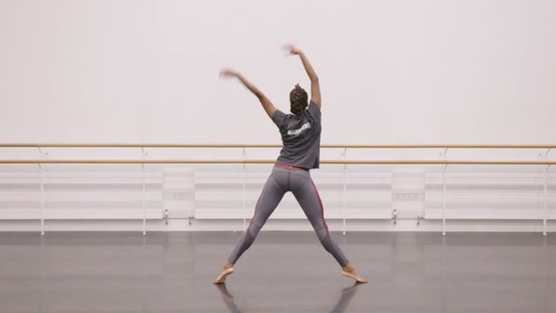 A dancer in a grey outfit is doing a pose in a dance studio.