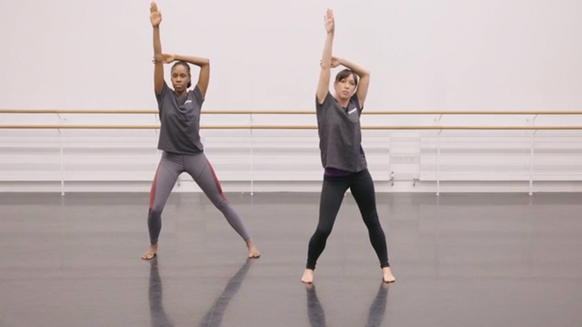 Two dancers in a dance studio with their arms raised.