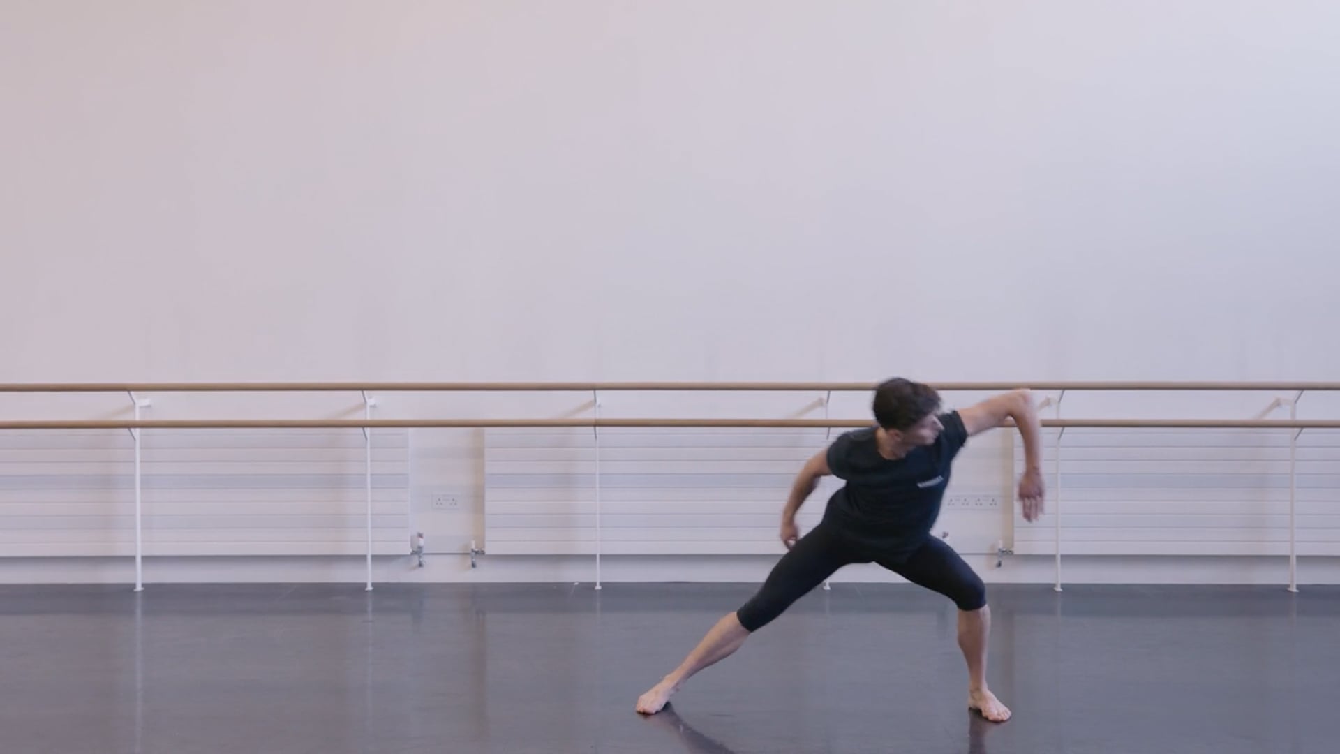 A dancer in a black top and black shorts in a dance studio.