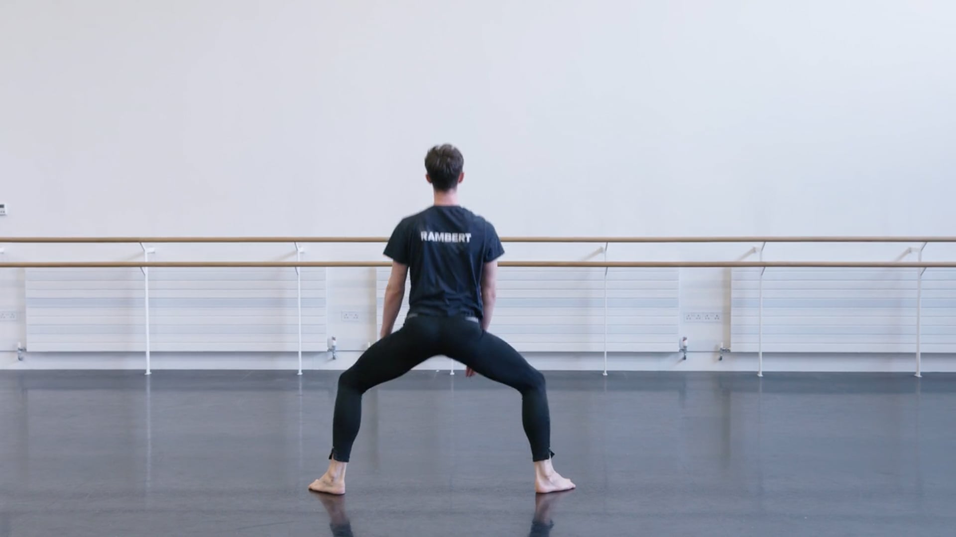 A man in a black shirt is standing in a dance studio.