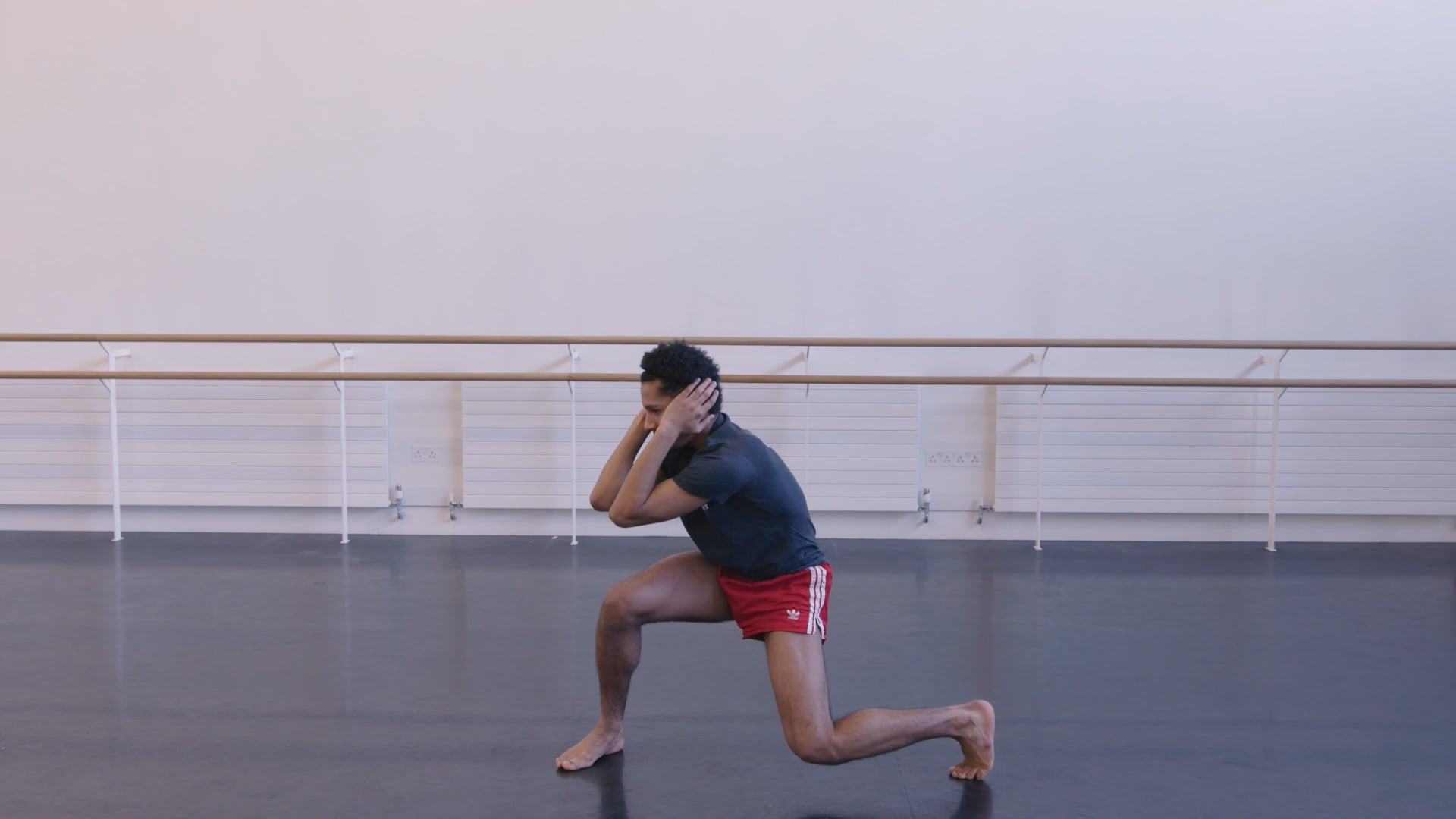 A man squatting in a dance studio.