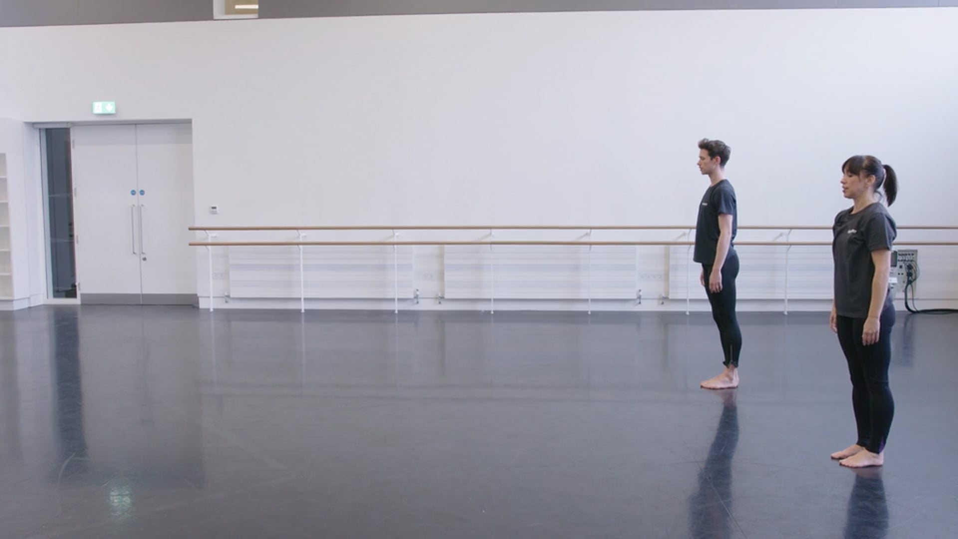 Two dancers standing in an empty dance studio.