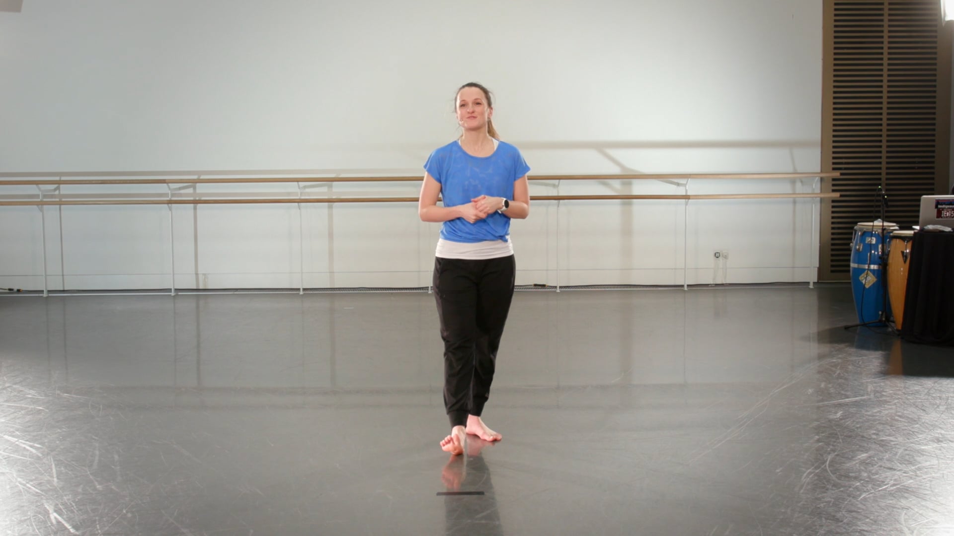 a woman in a blue shirt is standing in a dance studio.