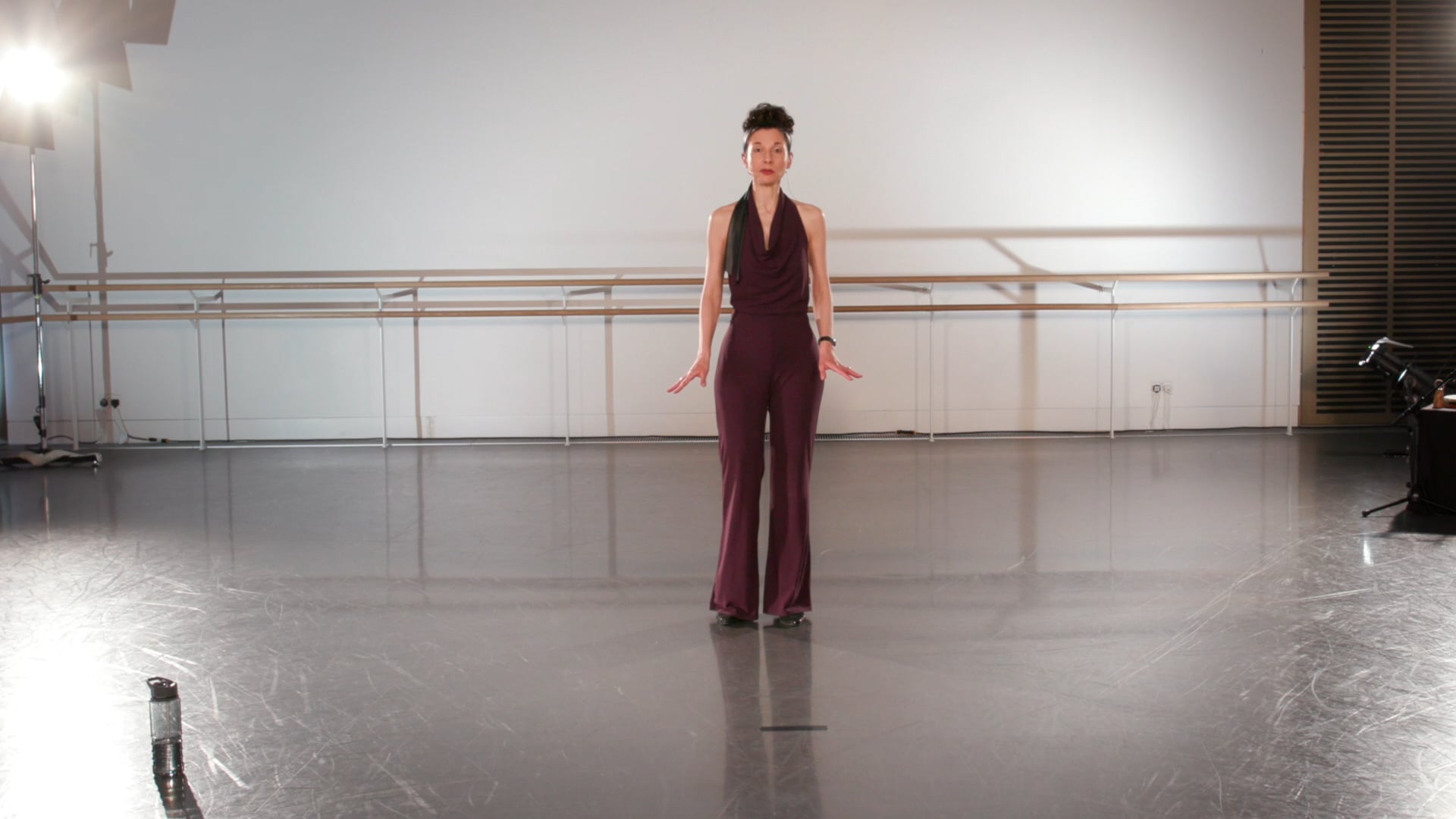 a woman standing in a dance studio with her arms outstretched.