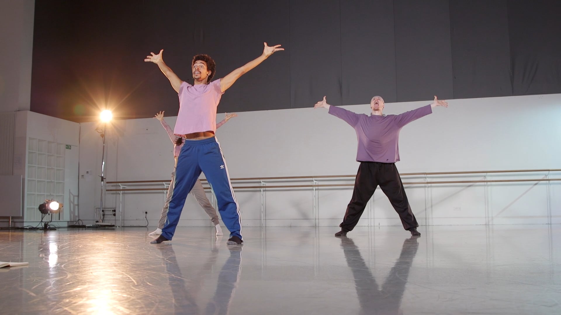 three people in a dance studio with their arms in the air.
