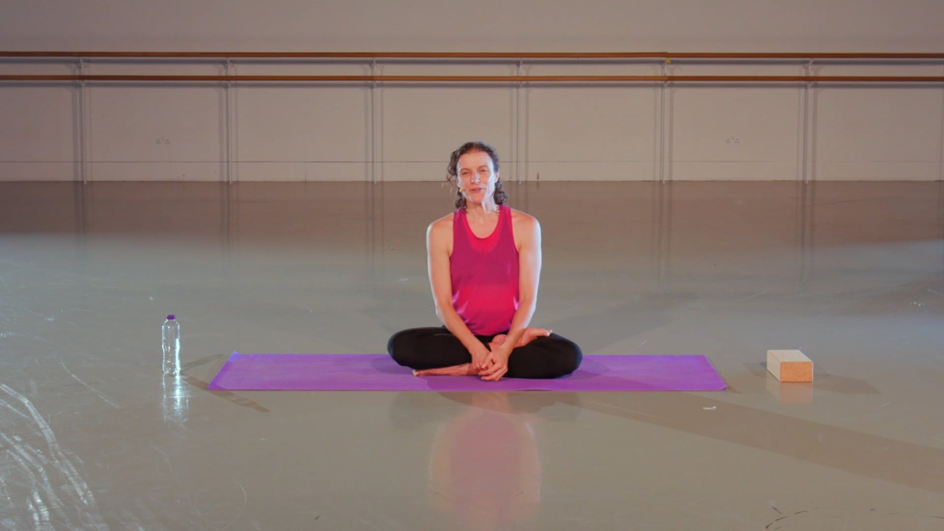 a woman sitting on a yoga mat in a gym.