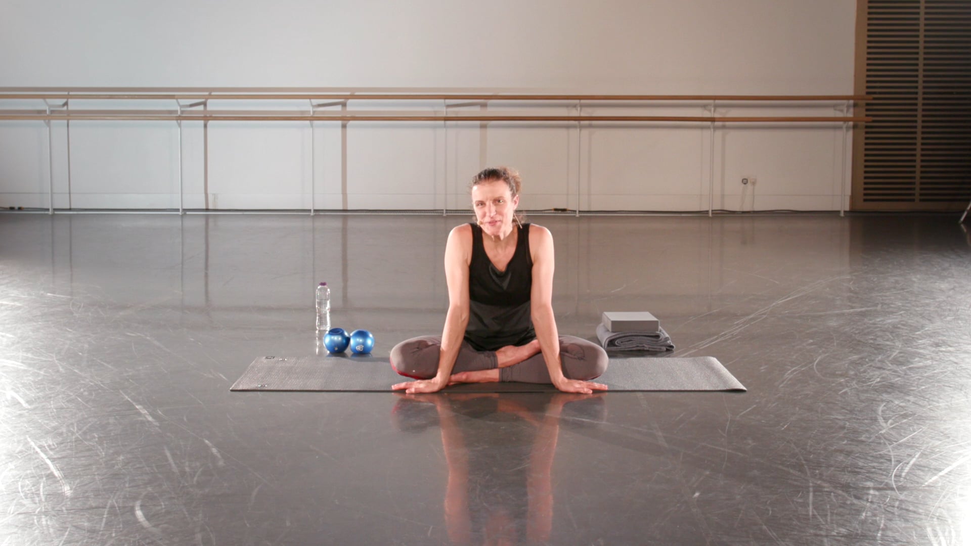 a woman sitting on a yoga mat in a gym.
