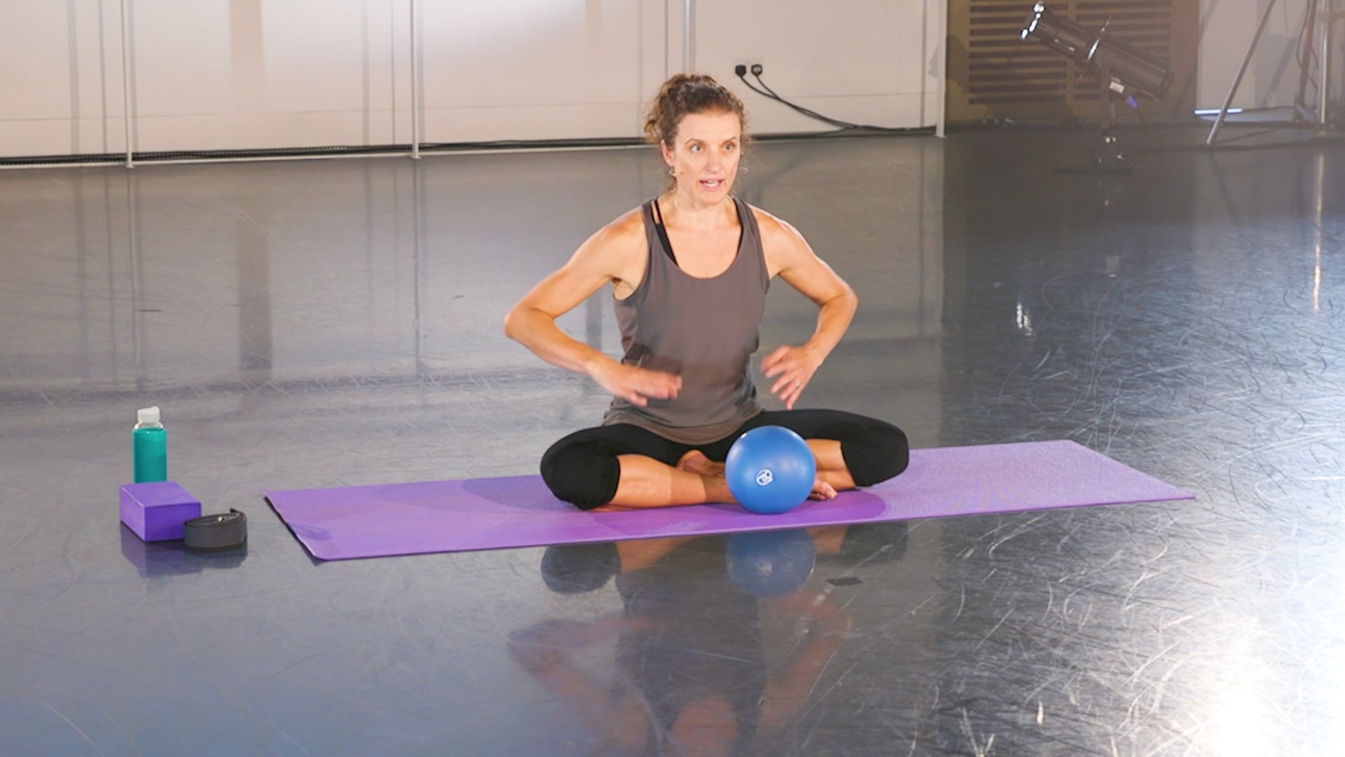 a woman sitting on a yoga mat with a blue ball.