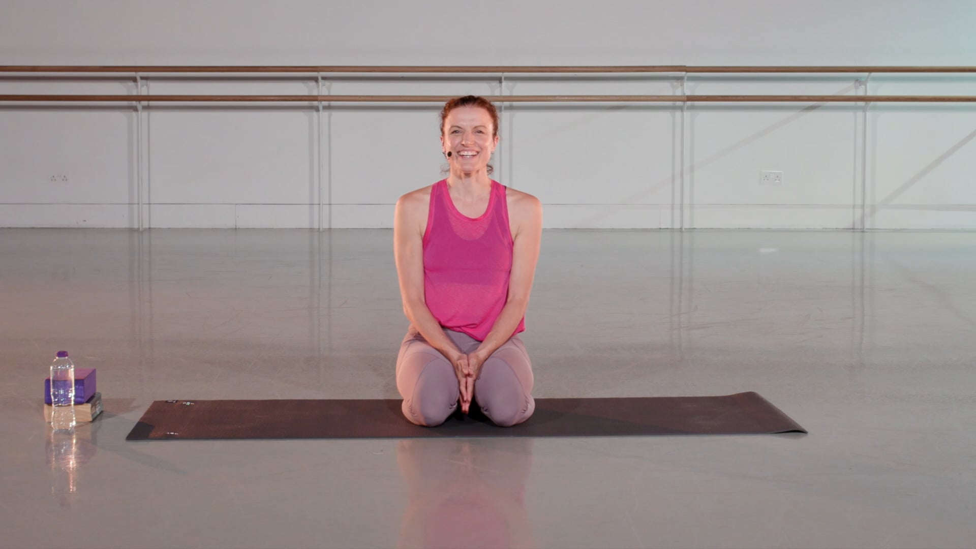 a woman sitting on a yoga mat with a bottle of water.