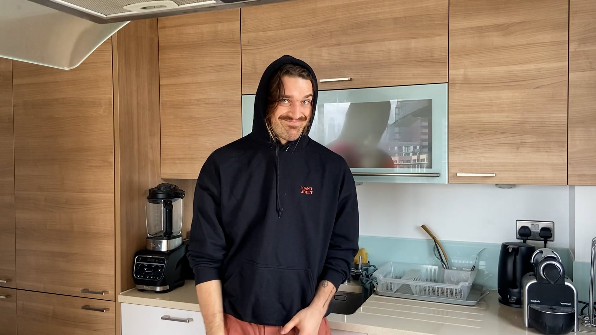 a man in a black hoodie standing in a kitchen.