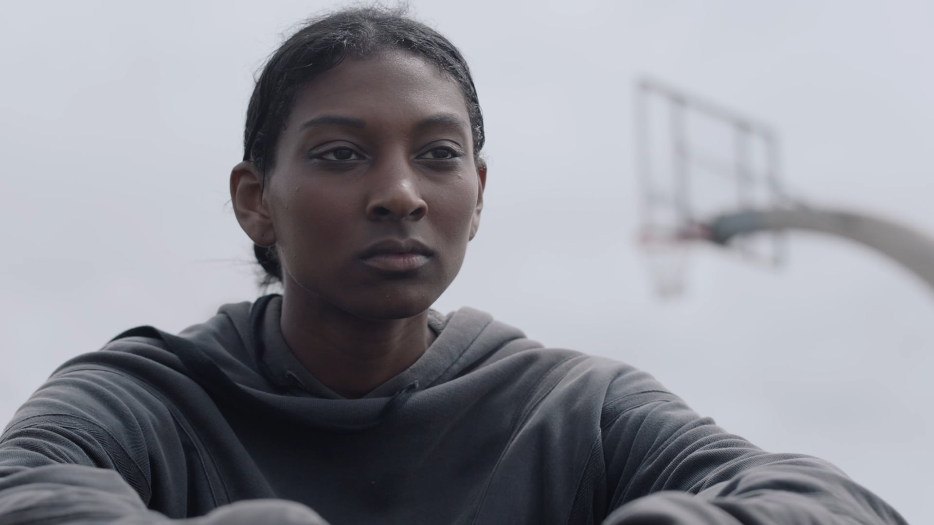 a woman in a gray hoodie standing in front of a basketball hoop.