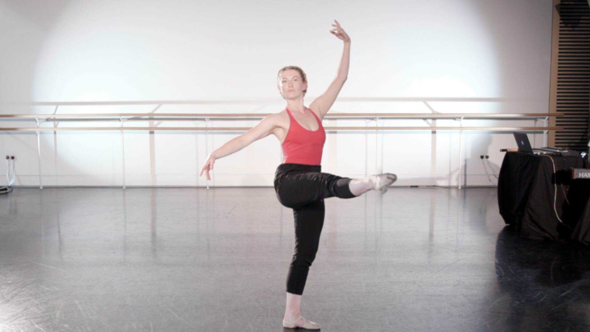 a woman in a red tank top is doing a ballet move.