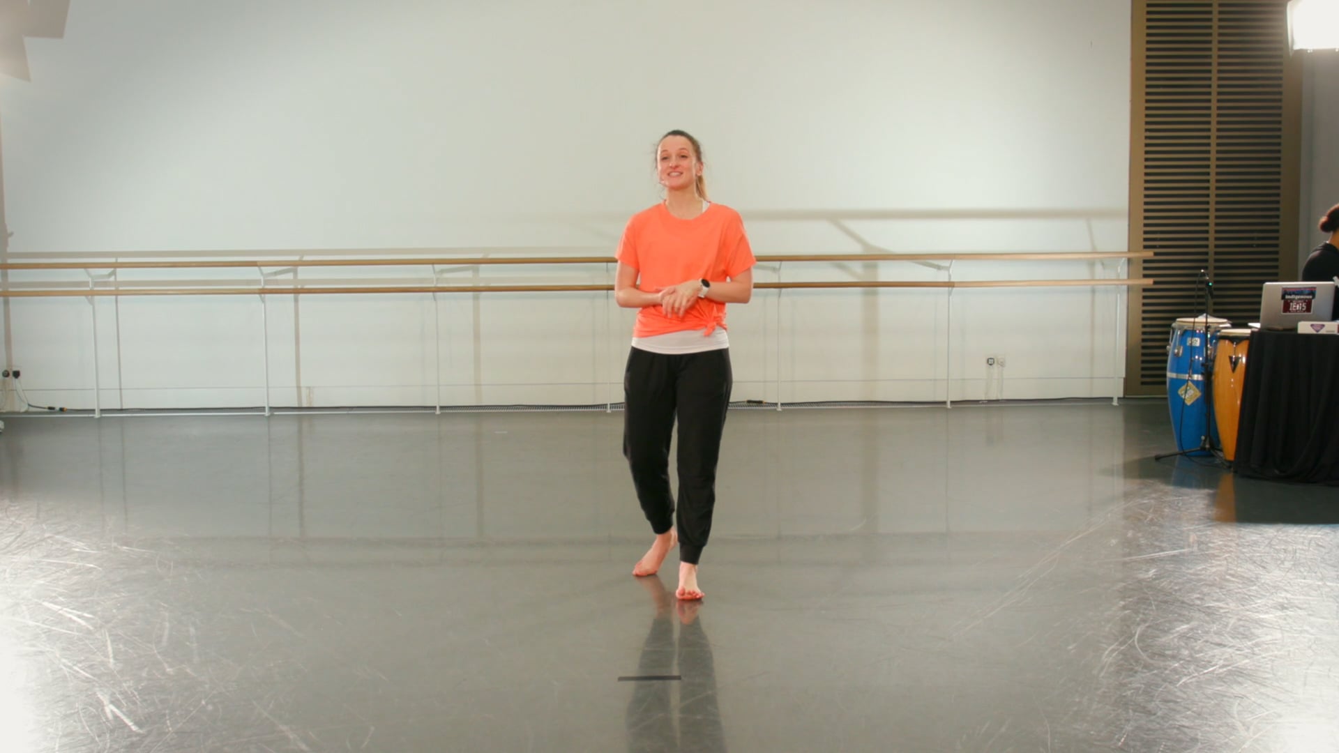 a woman in an orange shirt is standing in a dance studio.