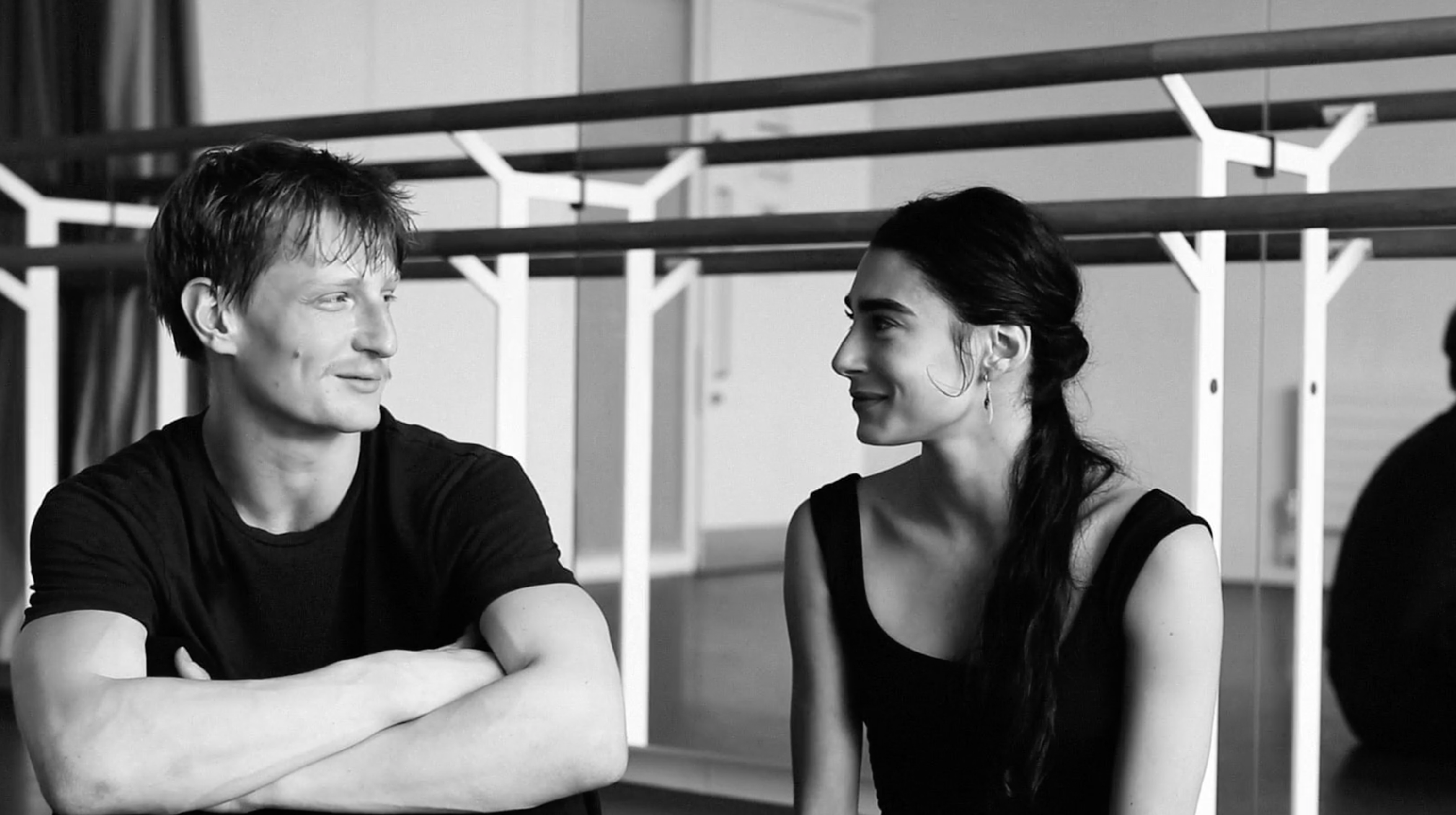 A male and a female dancer sitting in the studio talking to each other and sharing their experience during a production rehearsal