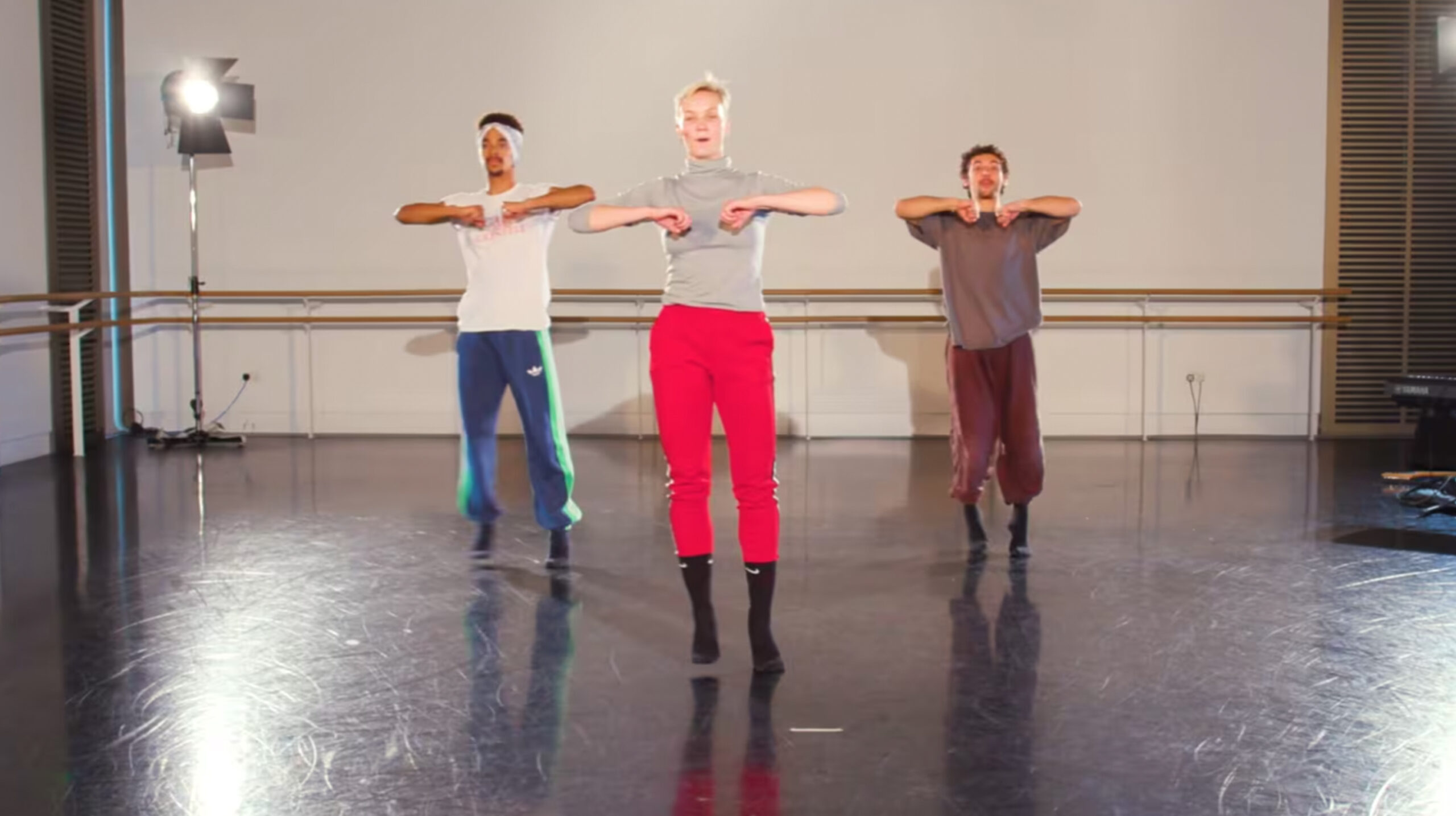 A dancer with red trousers and grey t-shirt heading a class inside a studio, while two other dancers are following her as a leader