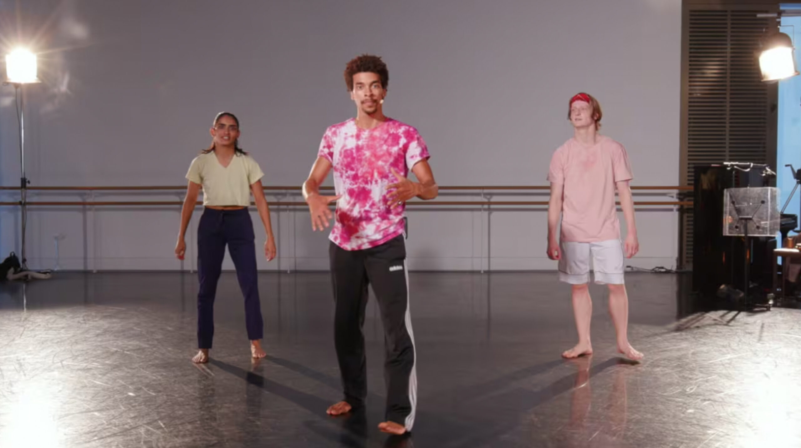 Teacher with a pink and white shirt with two other dancers behind him inside a studio