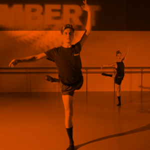 A male ballet dancer leading a class with his arms up and one of his legs pointing out to the back