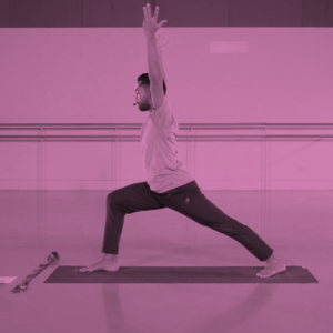 Male yoga teacher during a class and in a pose with a mat underneath him.