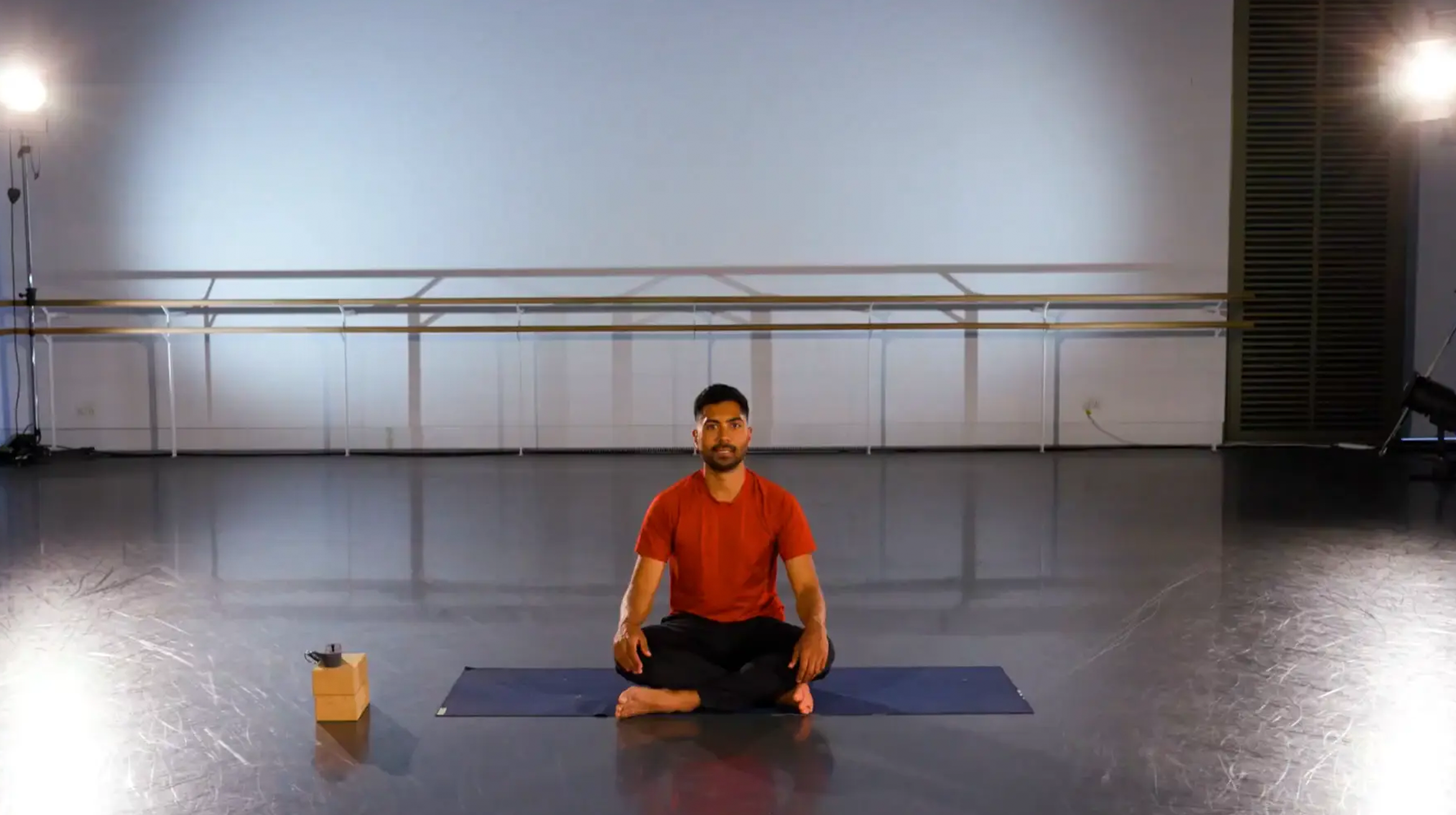 Yoga teacher with a pink shirt sat with a mat underneath him.