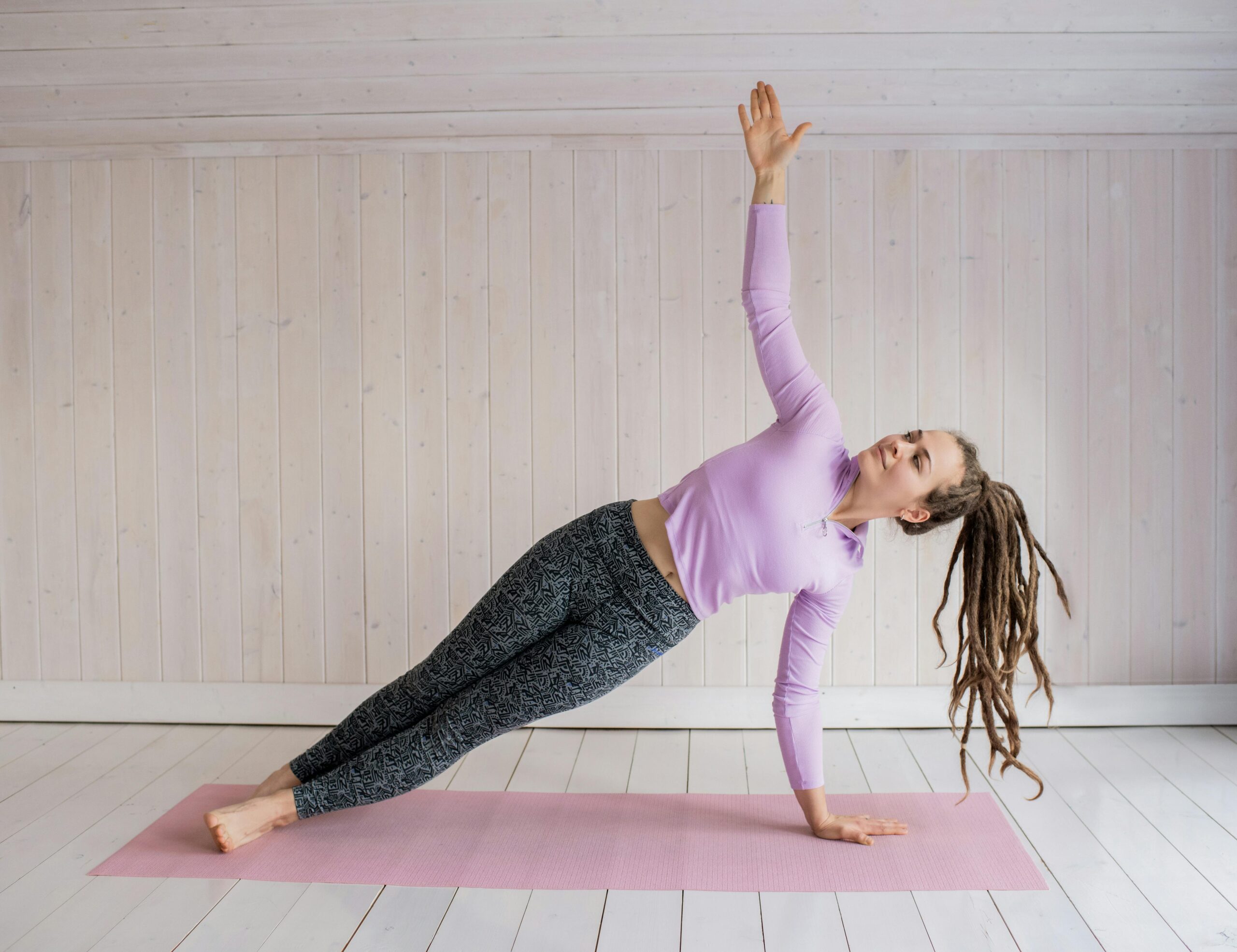 Woman in her 30s doing a Pilates exercise on a pink mat