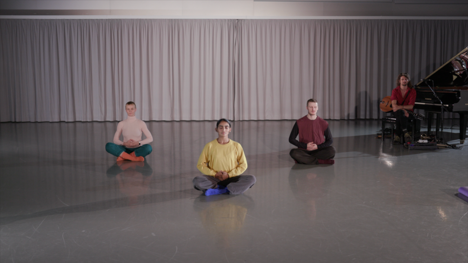 Yoga teacher and students sat on the floor inside a studio with sweaters with different colours